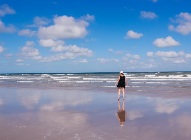 Woman on deserted beach wearing black dress and hat