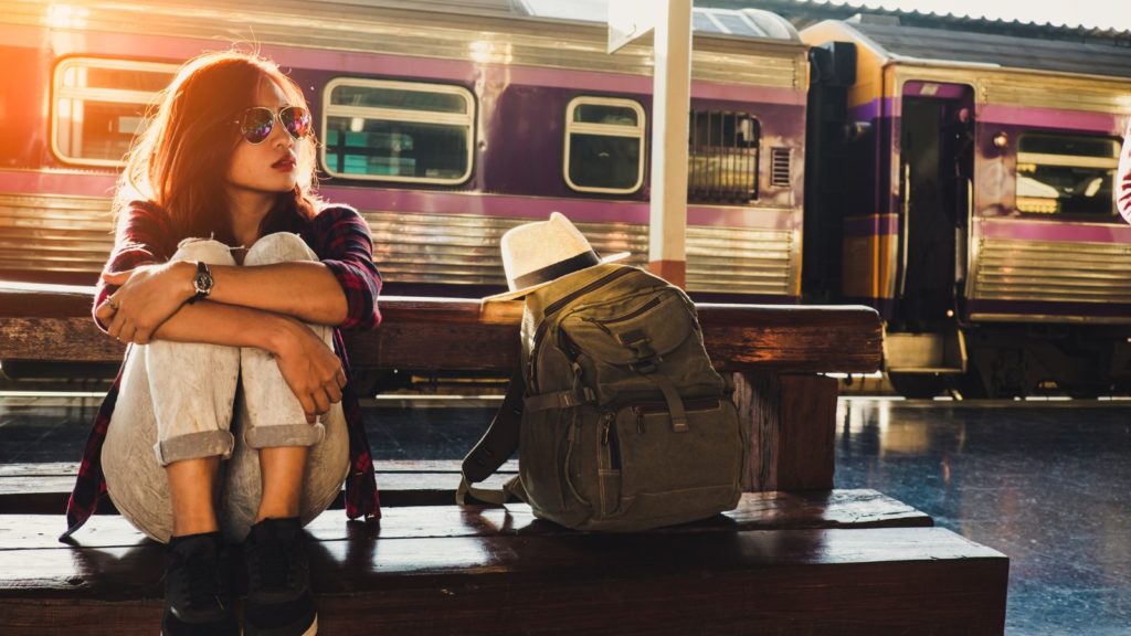Solo travel traveler sitting near a train with a backpack.