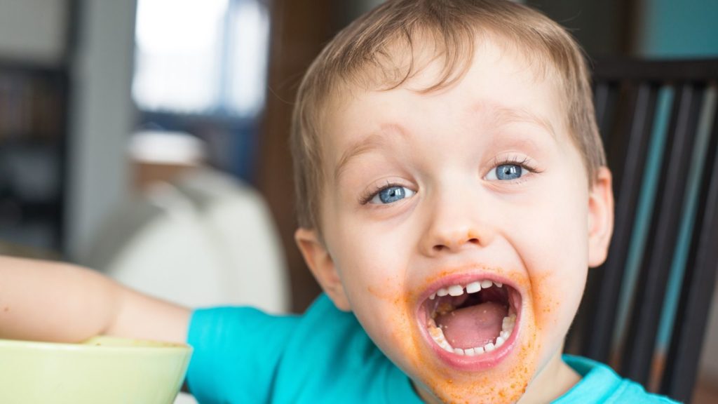 Close up of little boy with sauce on his face.