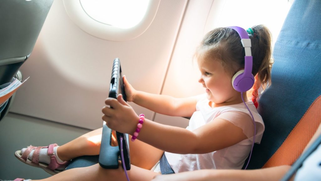 Child on an airplane with headphones and iPad.